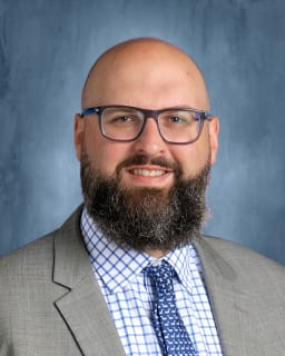 Photo of Mr. Chairge in a suit with glasses and a beard