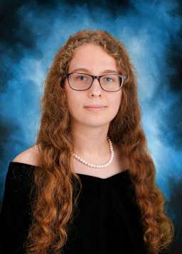 The image shows a young woman with curly red hair and glasses, wearing a black top, against a blue background with some smoke or haze.