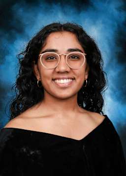 The image shows a young woman with curly dark hair and glasses, smiling warmly against a blue and smoky background.