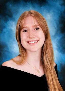 A smiling young woman with long, reddish-blonde hair stands against a blue, smoky background.