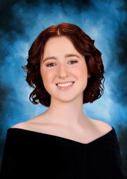 A young woman with curly brown hair and a warm smile, set against a vibrant blue background.