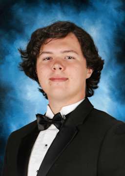 The image shows a young man wearing a black tuxedo with a bow tie, standing against a blue background with a slightly blurred effect.