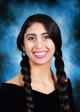 The image shows a young woman with long, dark braided hair, wearing a black top, and smiling against a blue background with some smoke or mist.
