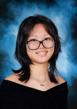 A smiling young woman with dark hair and glasses against a blue background.