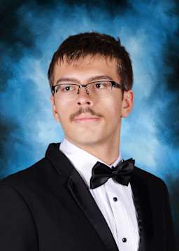 The image shows a young man wearing a black tuxedo with a bow tie, standing against a blue and smoky background.