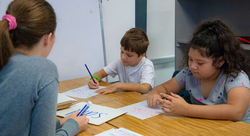A teacher works on reading skills with a young boy and young girl.
