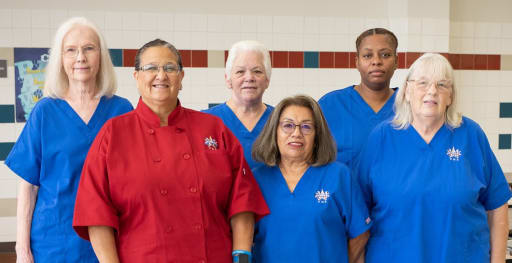 photo of 6 women wearing cafeteria smocks smiling at the camera