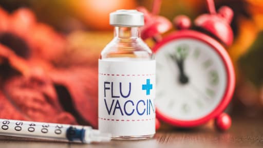 Flu Shot vaccine bottle and needle, with leaves and clock in the background