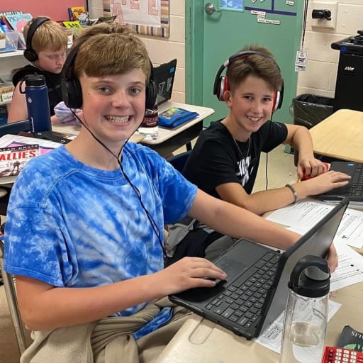 2 boys in class with headphones working on laptops