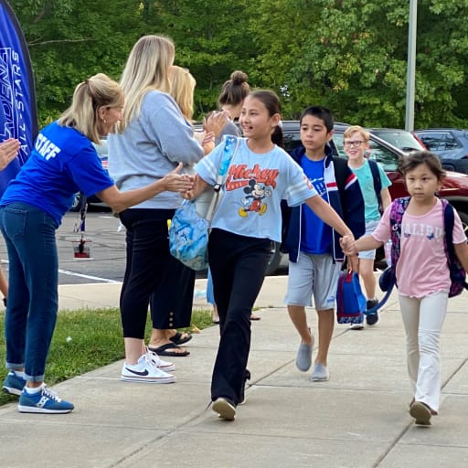 Outside on sidewalk, teacher giving a high five to a student during Fan Fair at Adena