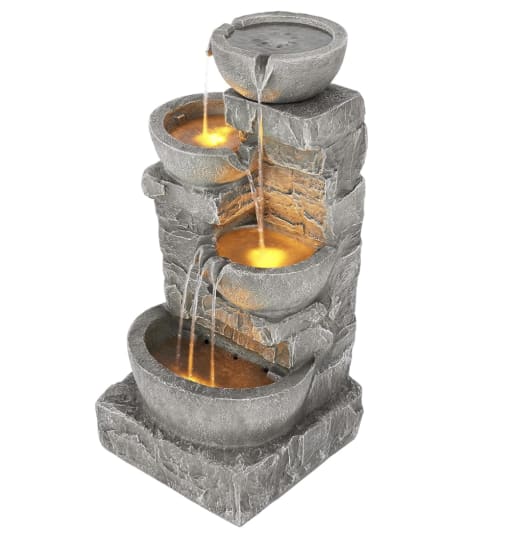 A four-tiered stone fountain with warm, glowing lights. Water cascades from top to bottom, creating a serene and tranquil atmosphere.
