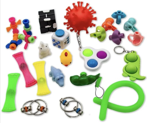 Assorted fidget toys including spinners, pop tubes, and stress balls are scattered on a white background, evoking a playful and colorful vibe.