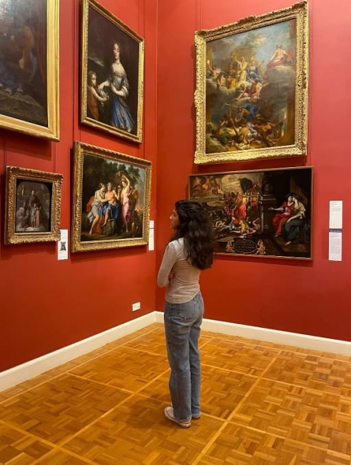 A high school girl studying abroad stands in a red room full of art at a museum