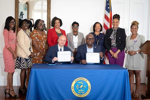 Governor Bryan and Secretary of Labor sign certificates, with VIDE and GVI administrators standing behind