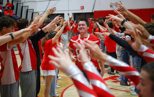 A group of people in red jerseys are gathered around a person in the center, raising their hands in celebration.