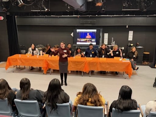 Woman stands in front of seated people in the foreground and background