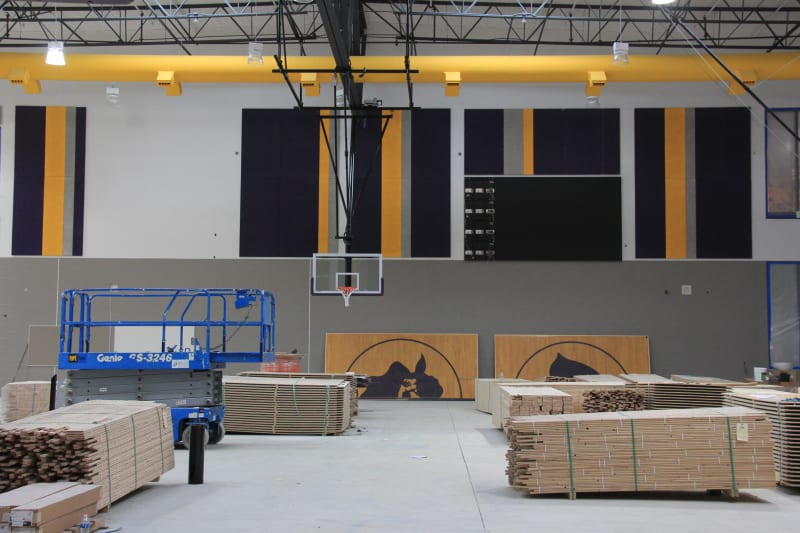 View of new HHS gym with yellow-gold ductwork, basketball hoop and piles of wood flooring.