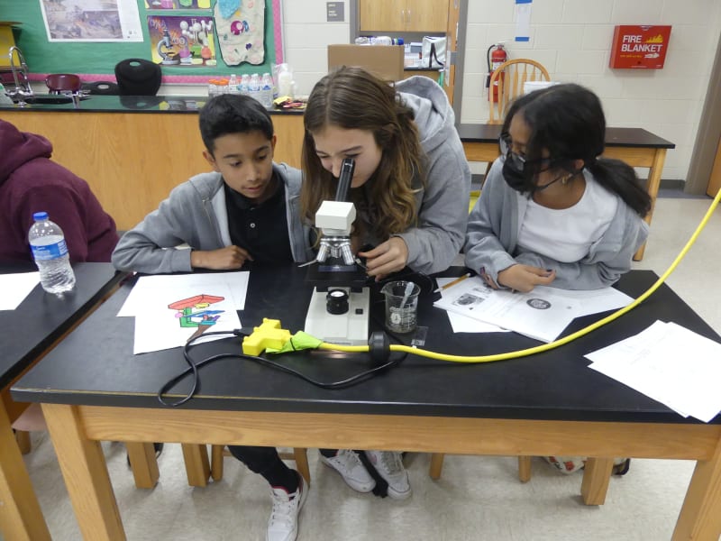 Three students at a table with a microscope
