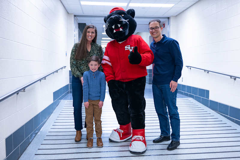 A photo of parents and their child smiling with a mascot Panther