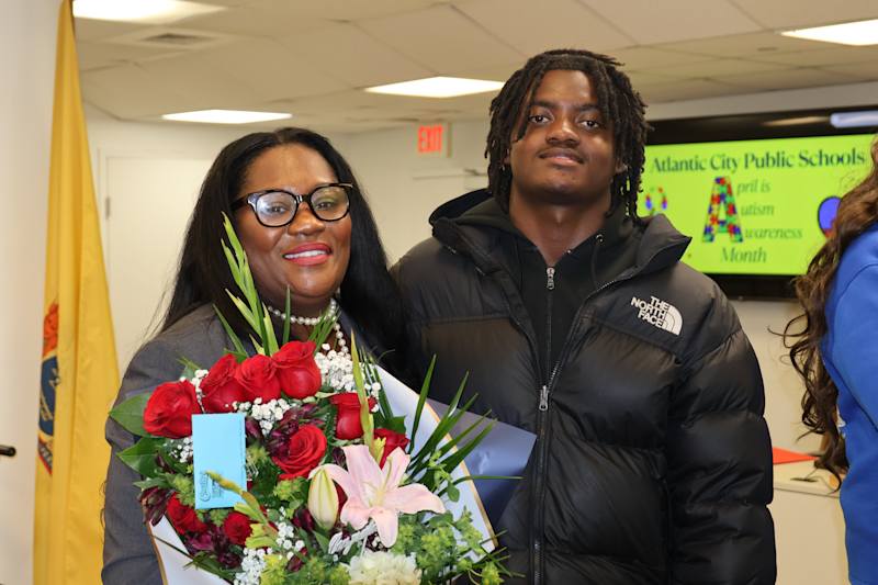 The image shows a woman and a man standing together, with the woman holding a bouquet of flowers. Th…