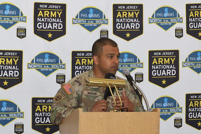 A man in a military uniform speaks at a podium in front of a backdrop featuring the New Jersey Army…