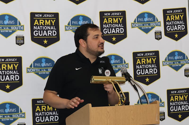 A man speaks at a podium in front of a backdrop featuring the "New Jersey Army National Guard" logo.