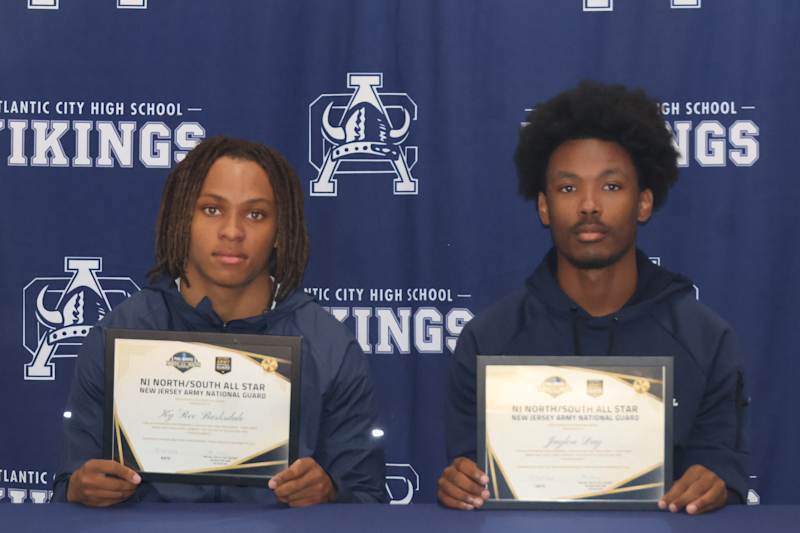 Two young men in navy jackets hold certificates in front of a backdrop with "Atlantic City High Scho…
