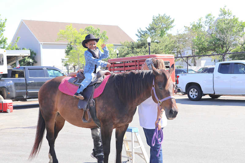 A young child in a cowboy hat waves from atop a horse with a pink saddle, while a person holds the r…