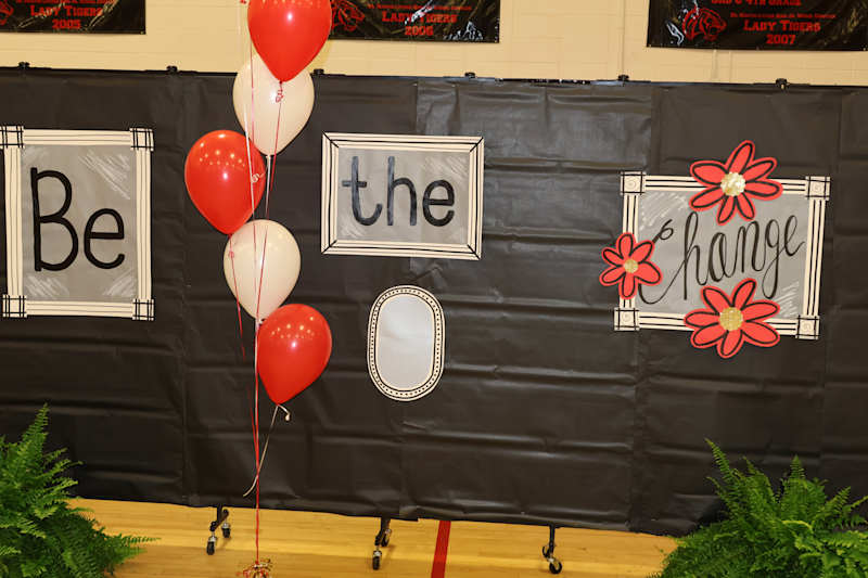 Red and white balloons float in front of a black backdrop displaying framed words "Be the change" an…