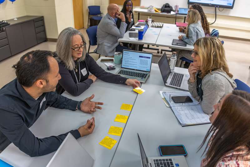 CMS educators collaborating with laptops and sticky notes during an active district AI training session.