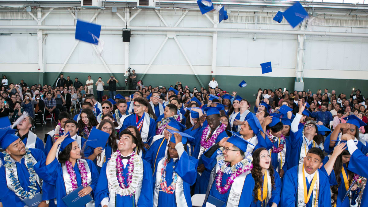 Students in graduation regalia throwing graduation caps into the air.