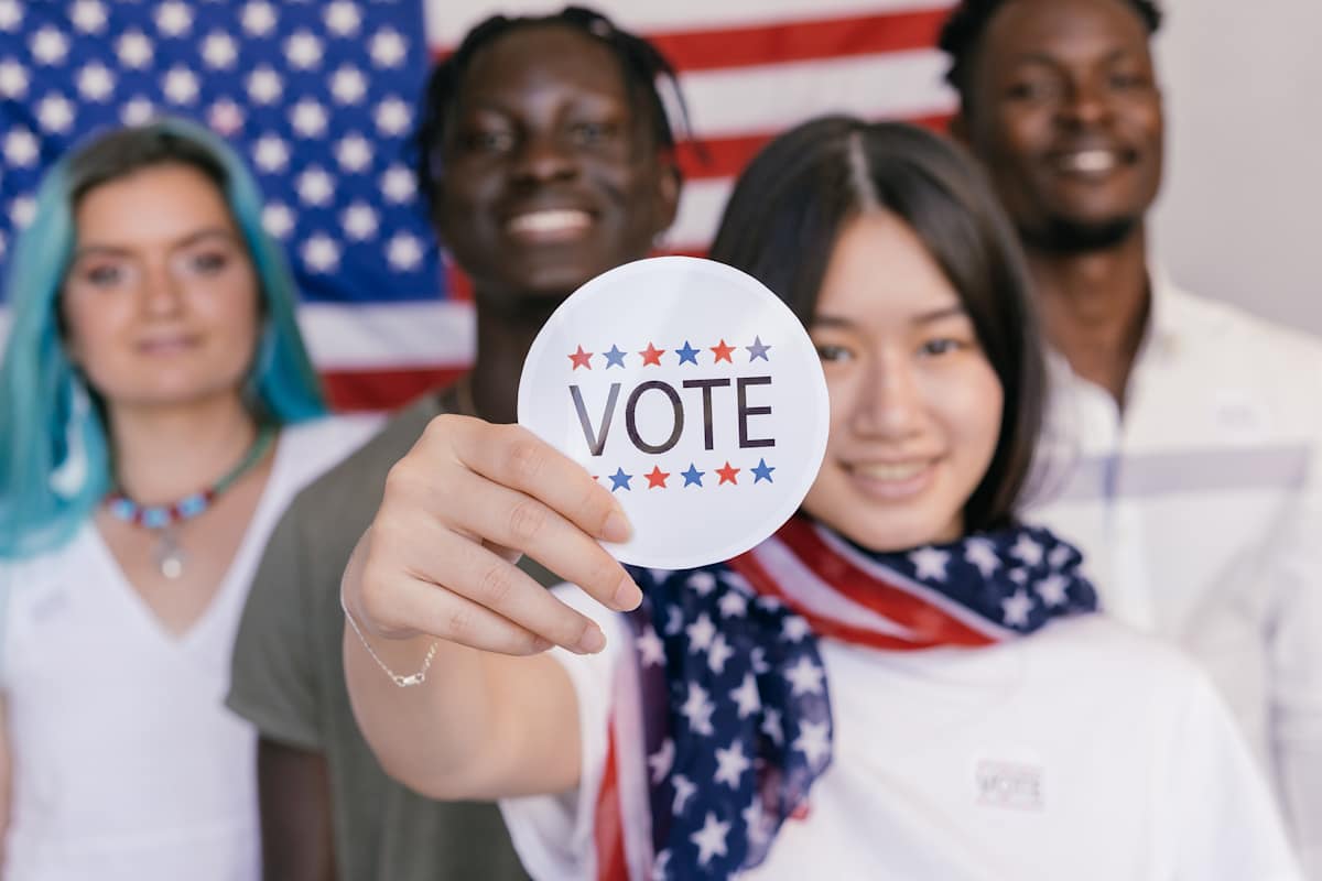 A digital art rendition of a group of young, racially diverse people holding up a "Vote" sticker