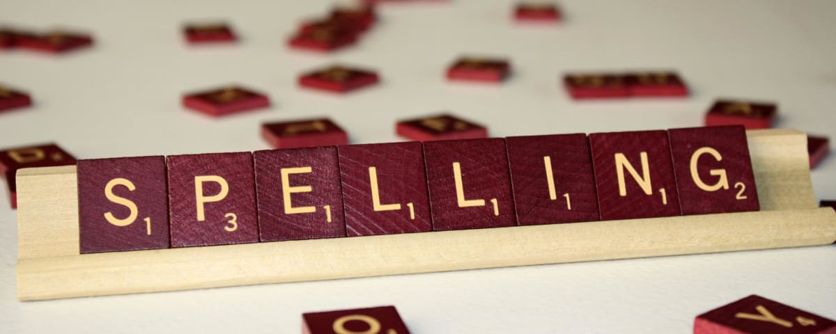 The image shows a set of Scrabble tiles spelling out the word "SPELLING" against a blurred background.