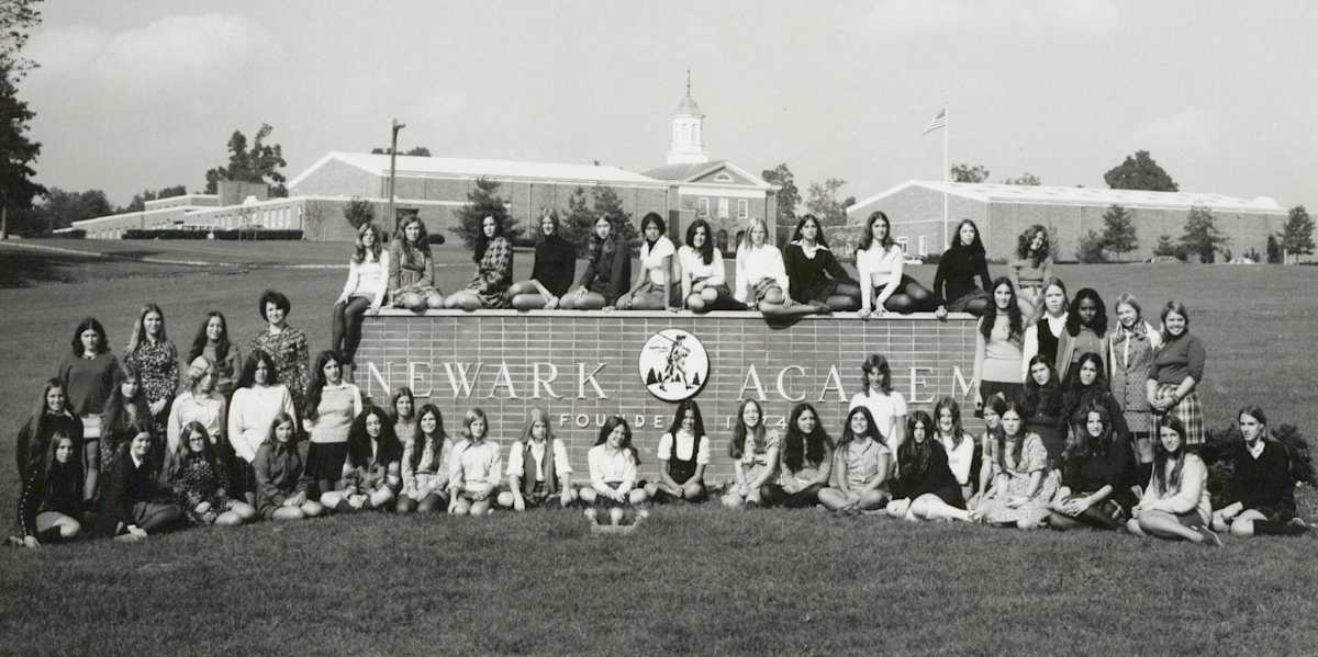 A group of female students sit by a Newark Academy sign
