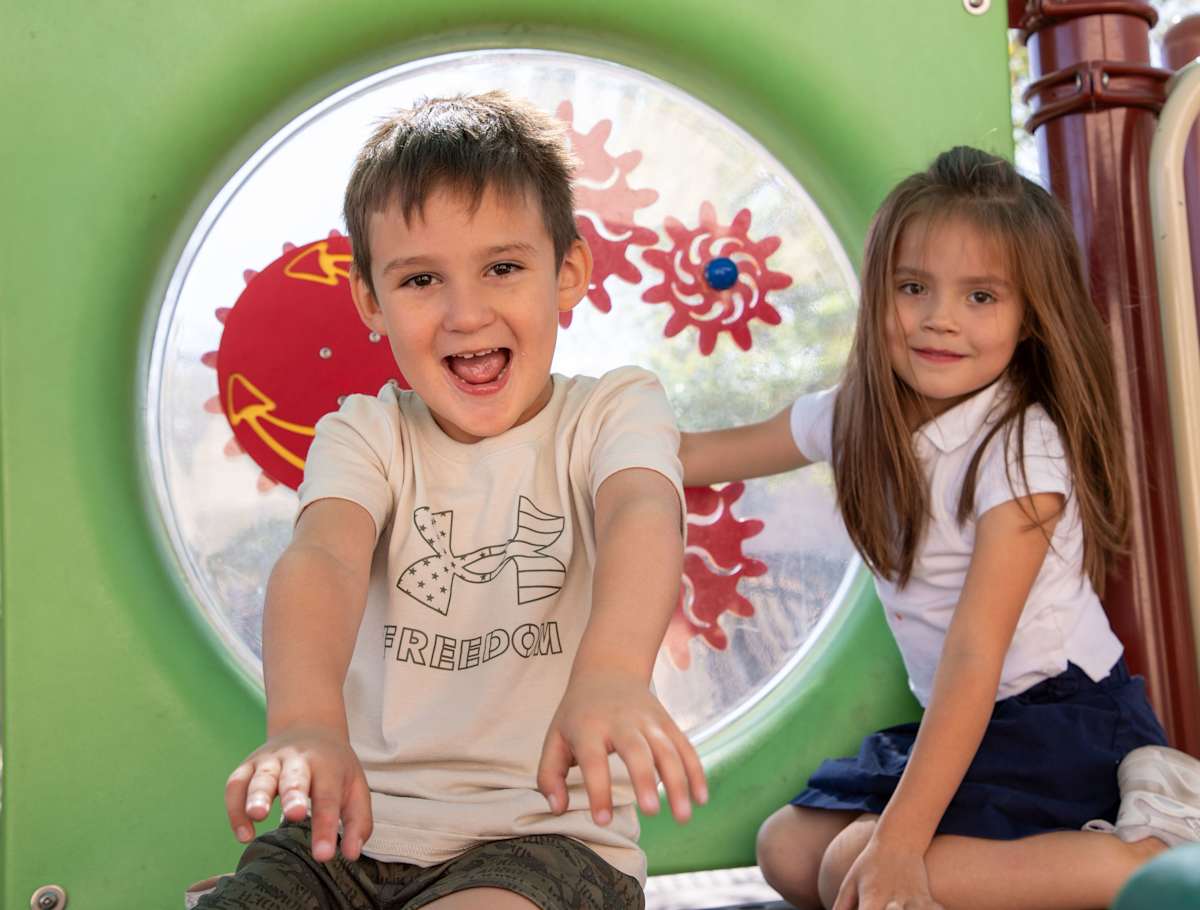 A boy and a girl are sitting on playground equipment similing
