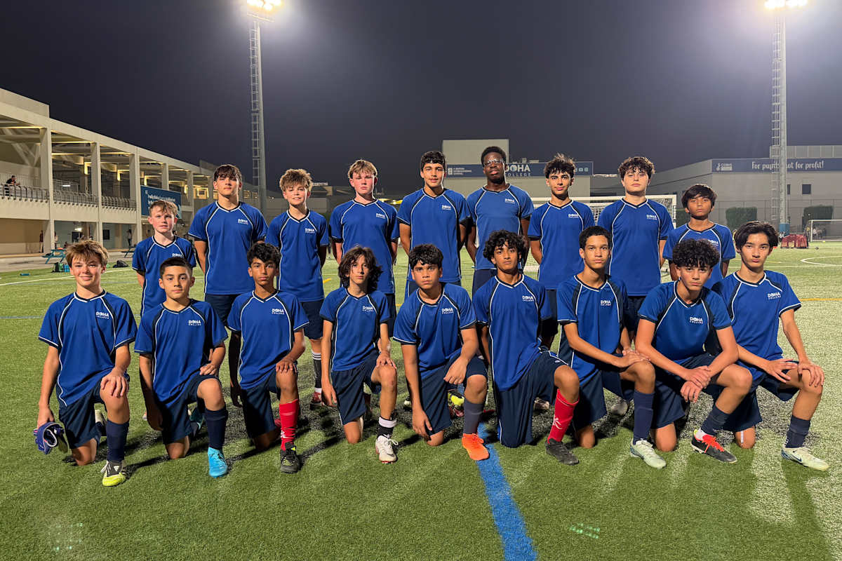 A group of young soccer players in blue uniforms posing together on a well-lit soccer field at night.