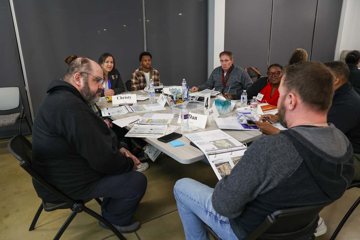 Participants gather around a table covered with planning materials during a committee meeting.