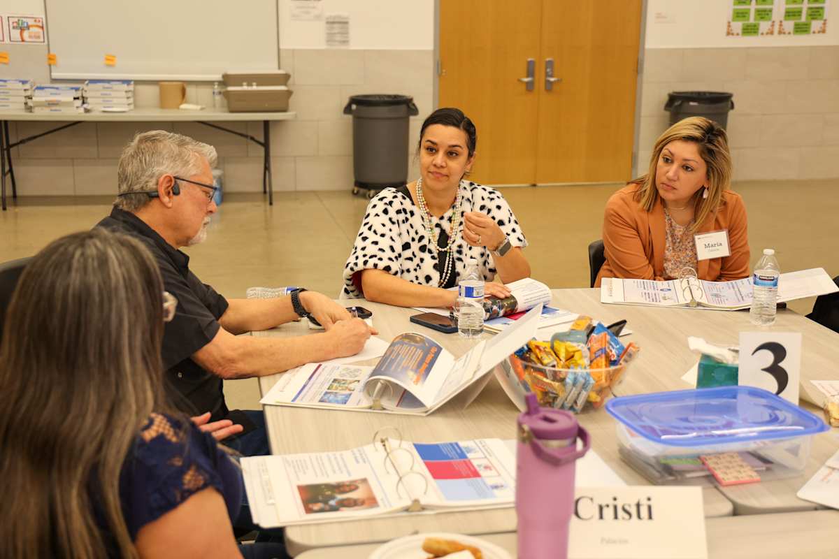 Committee members gather around a table with meeting materials during a planning discussion.