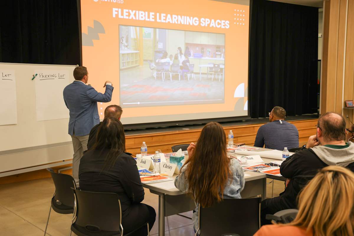 A presenter stands in front of a group while delivering a presentation on Flexible Learning Spaces.