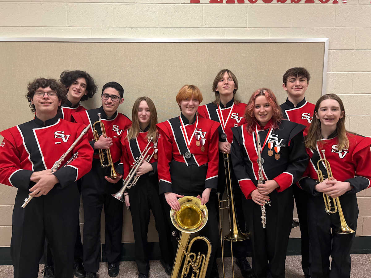 Student musicians in their outfits smiling with their instruments