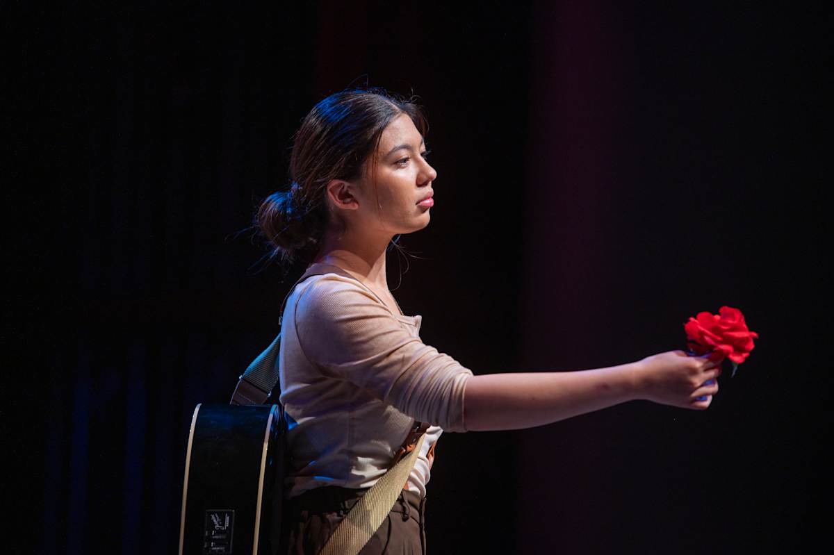 Student performing on stage with a red rose