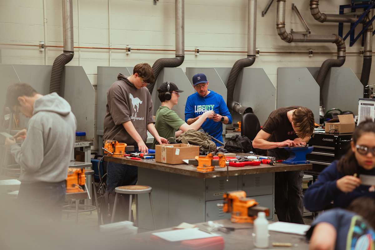 Students in a workshop are gathered around a workbench