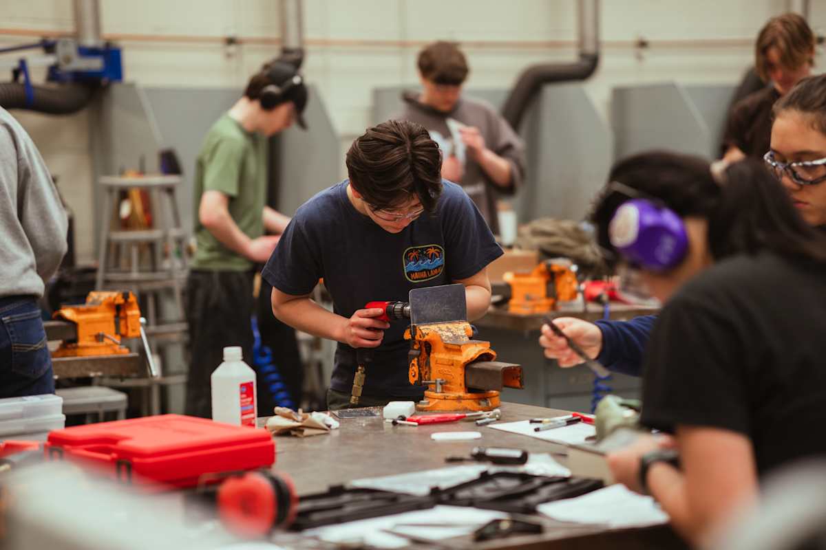Students work on projects at benches with vises and tools in a workshop