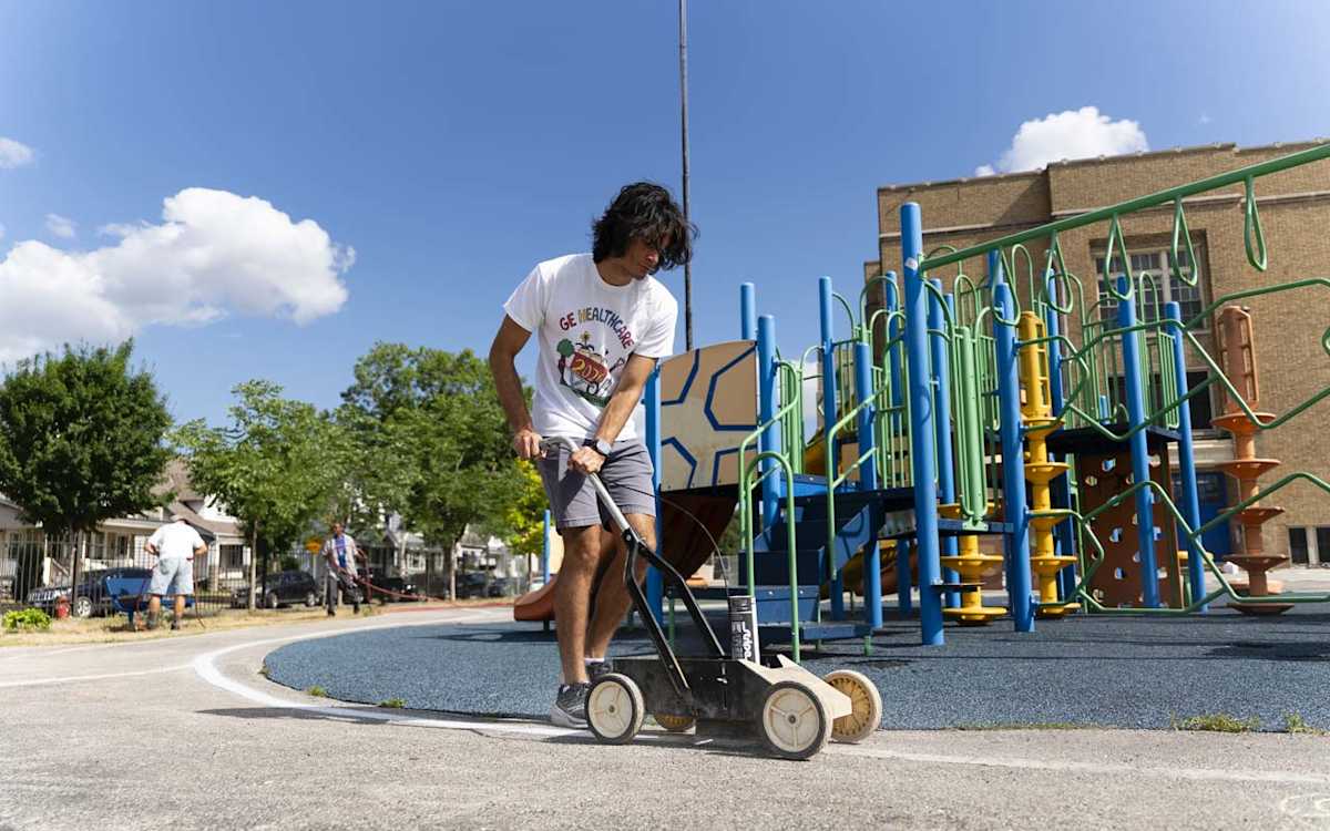 A GE HealthCare volunteer uses a striping machine to apply paint on the ALBA playground.