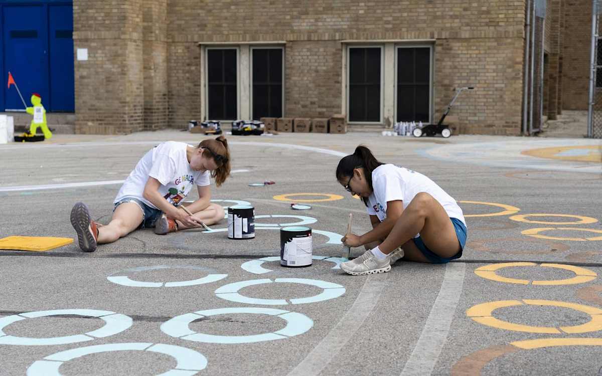 Two GE HealthCare volunteer paint circles by hand on the ALBA playground.