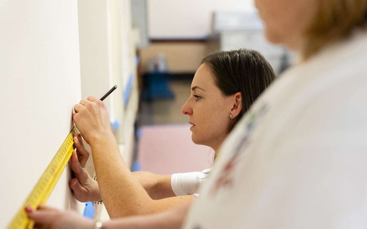 A GE HealthCare volunteer uses a ruler to prepare for painting inside ALBA.