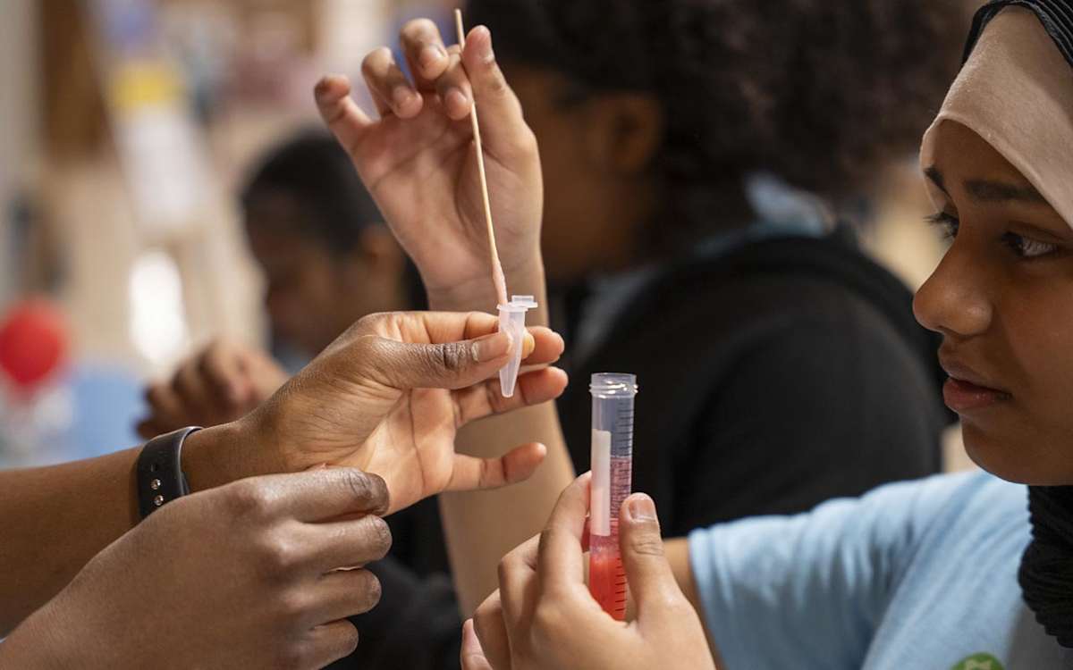 Two students conduct an experiment that involves transferring some liquid from a tube.