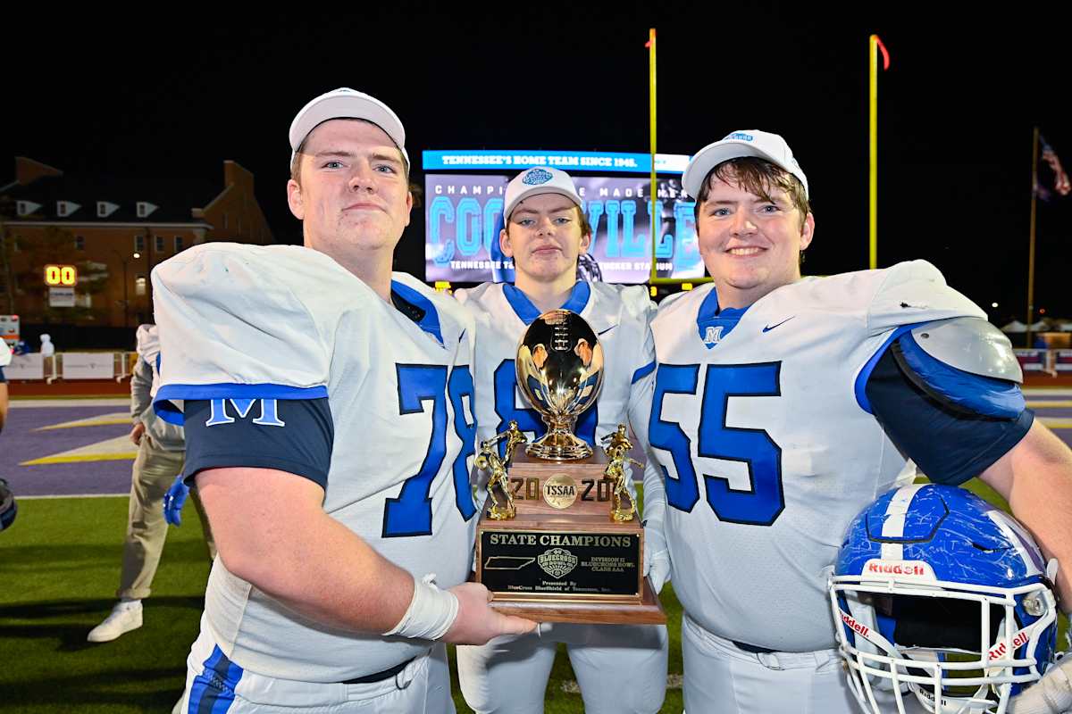 Three football players holding a trophy on a field.