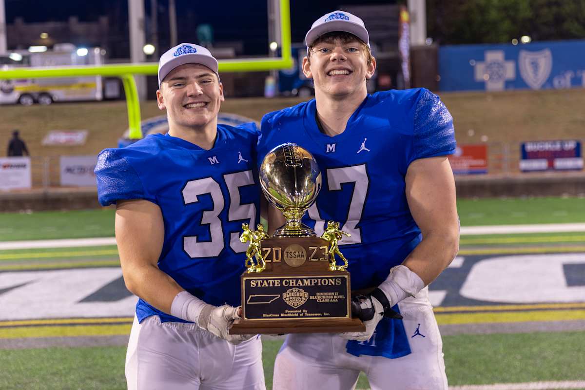 Two football players holding a trophy on a field.