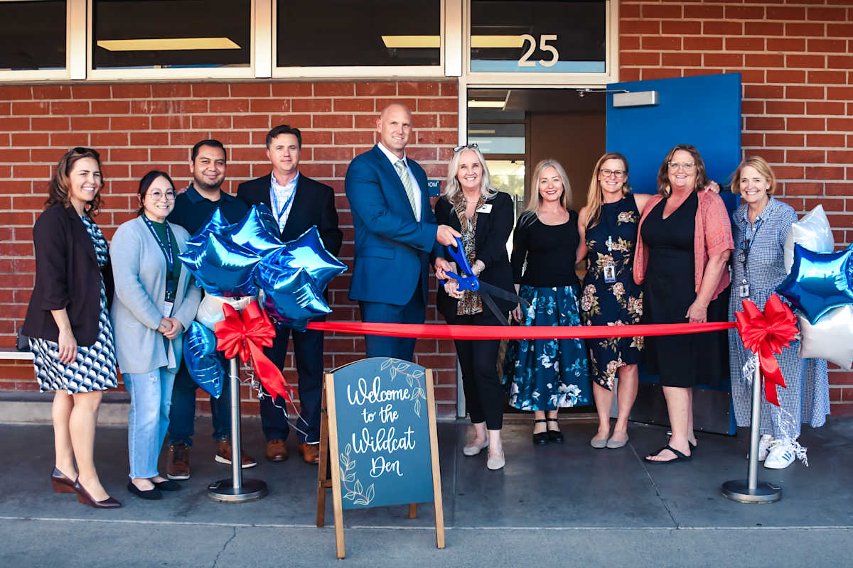 A group of admin and staff standing in front of a brick building for a ribbon cutting.